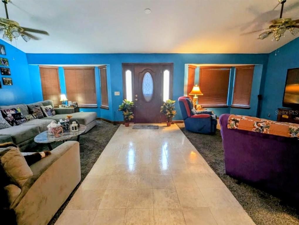 A living room features blue walls, a tiled entryway, carpeted seating areas, and two bay windows — 2220 EMPEROR DRIVE, KISSIMMEE, FL