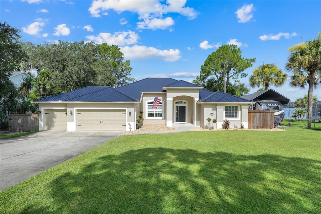 A single-story house with a blue metal roof, tan stucco exterior, and a three-car garage — 18233 ROSE STREET, GROVELAND, FL