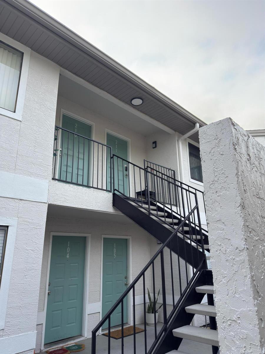 An exterior view of a two-story apartment building with teal doors and black metal stairs — 560 Breckenridge Village, FL 32714, FL