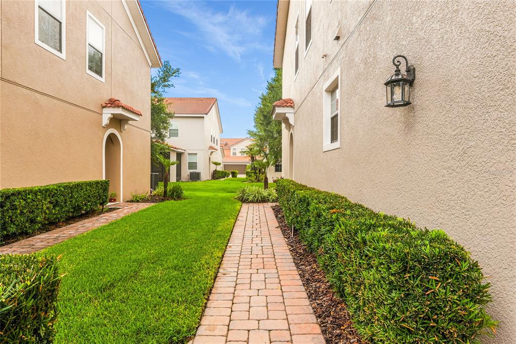 A brick walkway leads between two stucco houses with manicured hedges and green lawns — 5369 VIA APPIA WAY, SANFORD, FL
