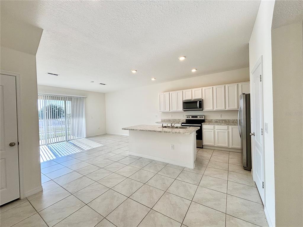 A kitchen with white cabinets, granite countertops, and an island opens to a tiled living area — 401 FELTRIM RESERVE BOULEVARD, DAVENPORT, FL