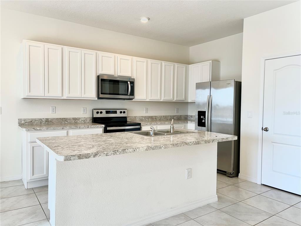 A kitchen features white cabinets, a granite-look island, stainless steel appliances, and tile flooring — 401 FELTRIM RESERVE BOULEVARD, DAVENPORT, FL
