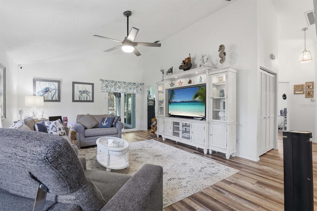 A living room features a white entertainment center, gray sofas, a patterned rug, and wood-look flooring — 86 HIGHLAND ROAD, TARPON SPRINGS, FL