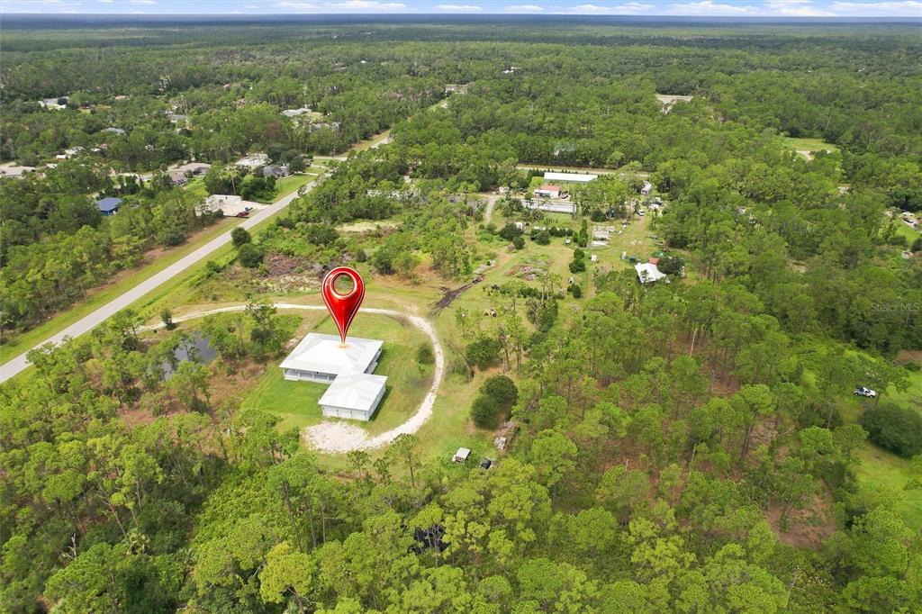 An aerial view shows a house with a white roof surrounded by trees and grass — 8146 TROPICAIRE BOULEVARD, NORTH PORT, FL