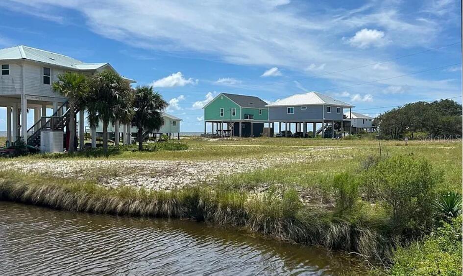 Several elevated houses stand near a grassy lot and a body of water — 3 MARLIN STREET, PANACEA, FL