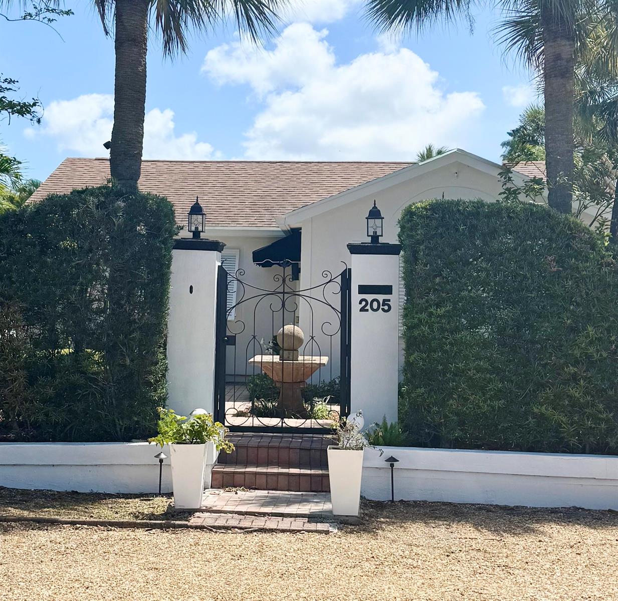 A white house entrance features a black metal gate, stone fountain, and tall hedge walls — 205 N 18th Ave Avenue N, FL 33460, FL