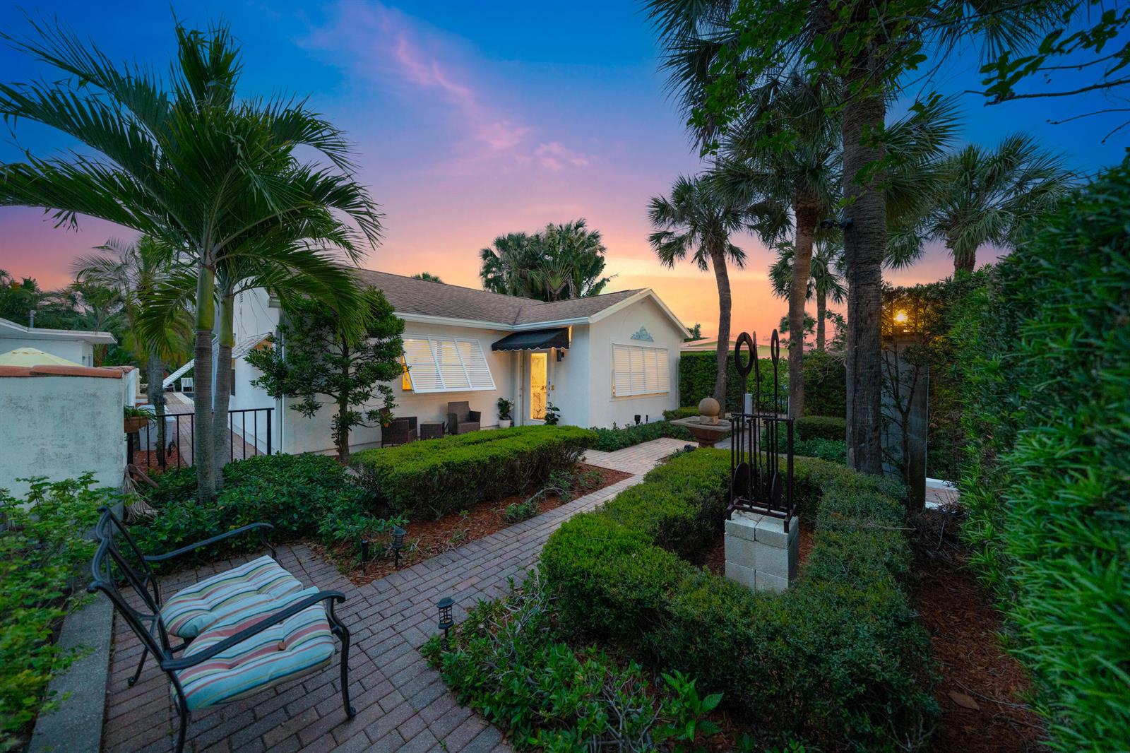 A white house with a brick walkway, manicured hedges, and palm trees at sunset — 205 N 18th Ave Avenue N, FL 33460, FL