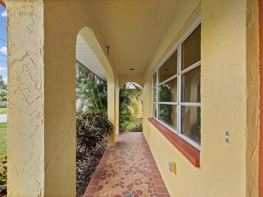 A covered outdoor walkway features yellow stucco walls, a tiled floor, and large windows — 1547 ANDOVER DRIVE, DUNEDIN, FL