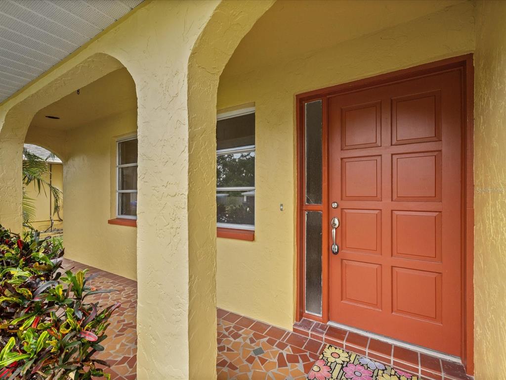 A yellow stucco house exterior features a red front door and a tiled porch floor — 1547 ANDOVER DRIVE, DUNEDIN, FL