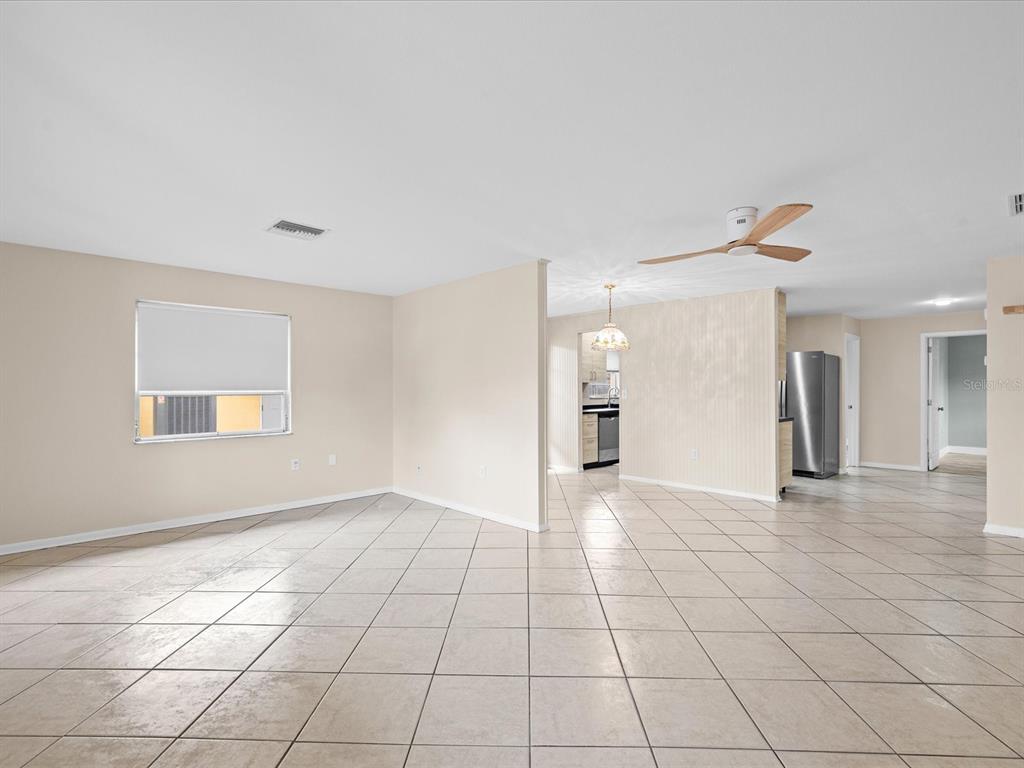 An open-concept living area features light-colored tile flooring, beige walls, and a ceiling fan — 1547 ANDOVER DRIVE, DUNEDIN, FL