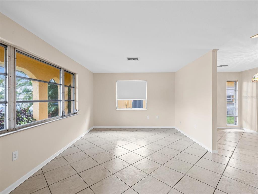 An empty room with beige walls, light-colored tile flooring, and multiple windows — 1547 ANDOVER DRIVE, DUNEDIN, FL