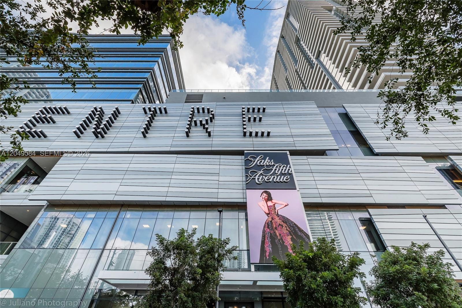 A low-angle exterior view shows the modern facade of a building featuring Saks Fifth Avenue — 88 SW 7th St # 2401, Miami FL 33130, MIAMI, FL