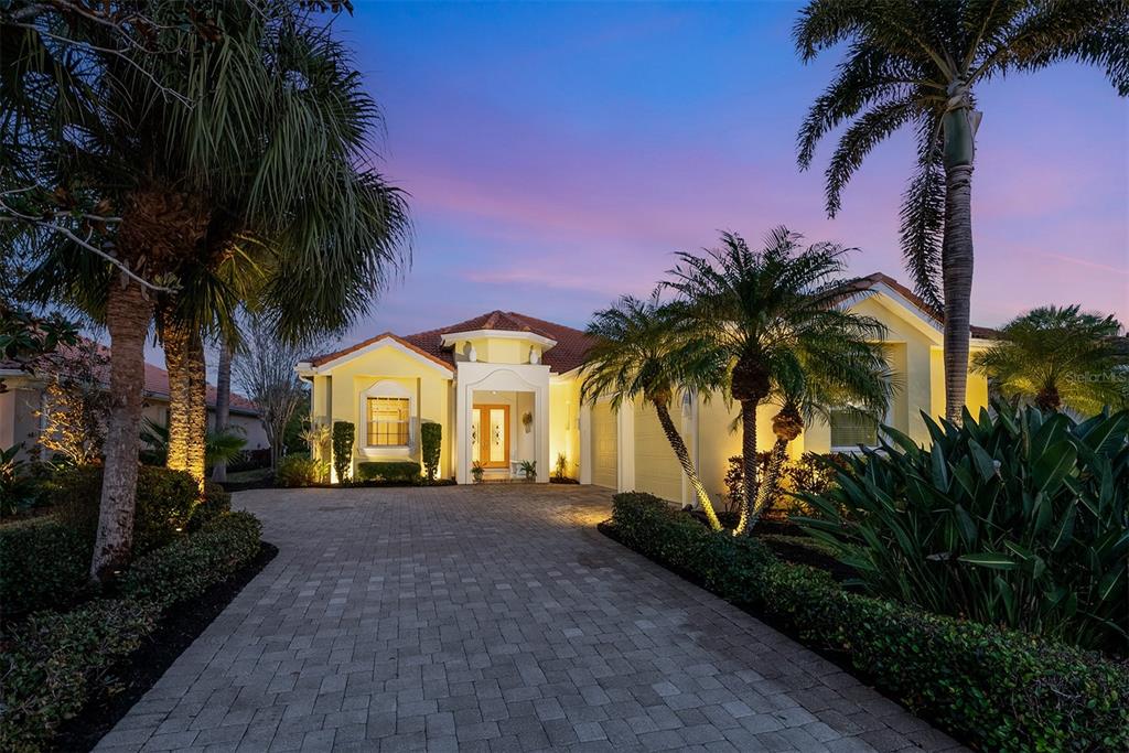 A single-story house with a paved driveway, palm trees, and yellow stucco exterior at dusk — 1752 GRANDE PARK DRIVE, ENGLEWOOD, FL