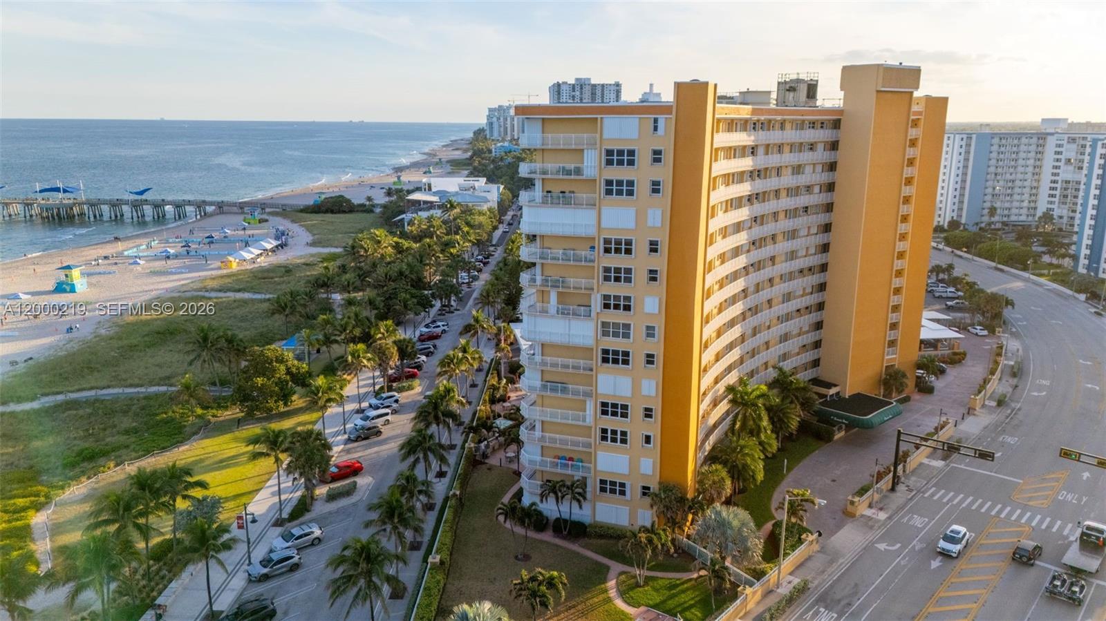 An aerial view shows a tall yellow apartment building near a beach and pier — 328 N Ocean Blvd # 707, Pompano Beach FL 33062, POMPANO BEACH, FL