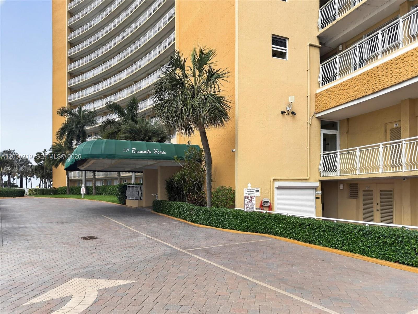A paved driveway leads to the covered entrance of a multi-story yellow apartment building — 328 N Ocean Blvd # 707, Pompano Beach FL 33062, POMPANO BEACH, FL