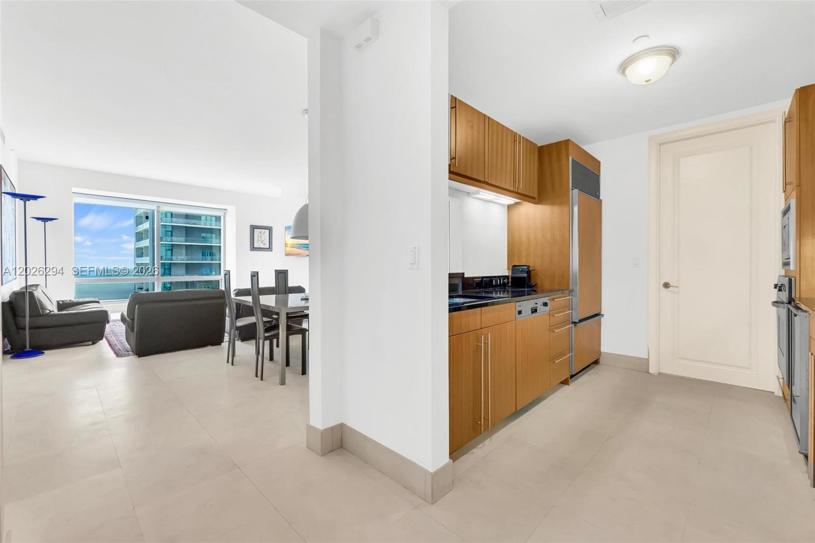 A modern kitchen with wood cabinetry opens into a living area with ocean views — 1425 Brickell Ave # 51A, Miami FL 33131, MIAMI, FL
