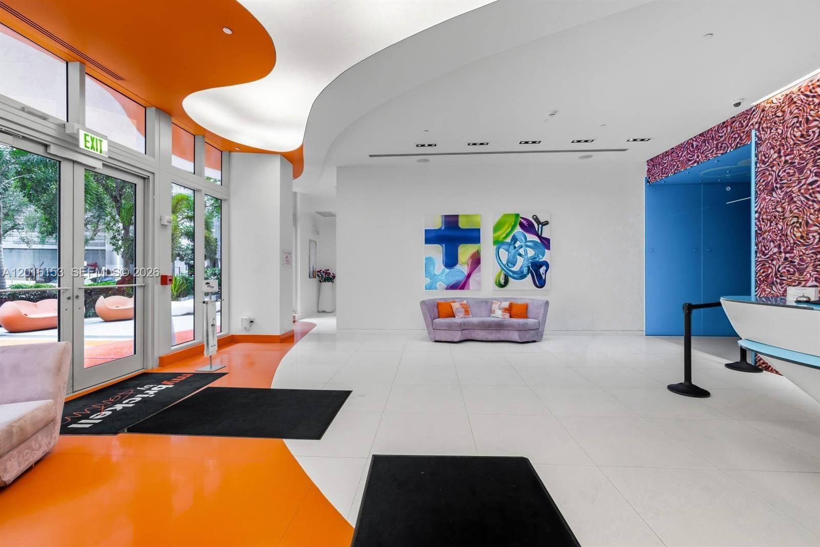 A modern lobby features white tile floors, orange accents, a purple sofa, and abstract art — 31 SE 6th St # 1904, Miami FL 33131, MIAMI, FL