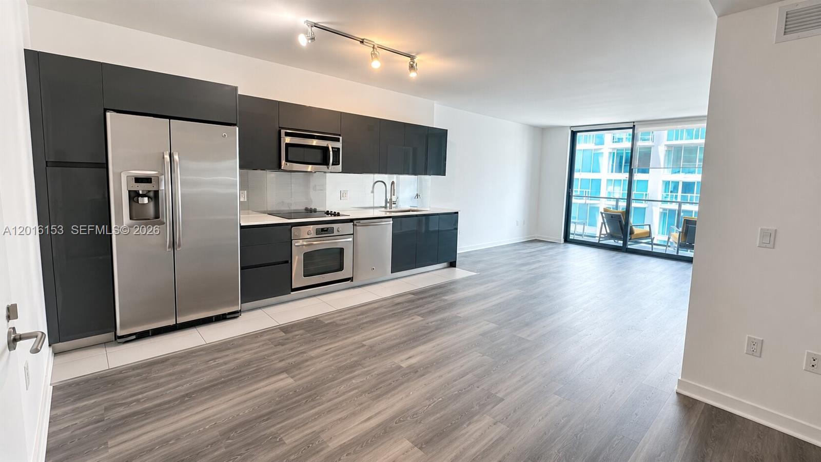 A modern kitchen with dark cabinets and stainless steel appliances opens to a living area — 31 SE 6th St # 1904, Miami FL 33131, MIAMI, FL
