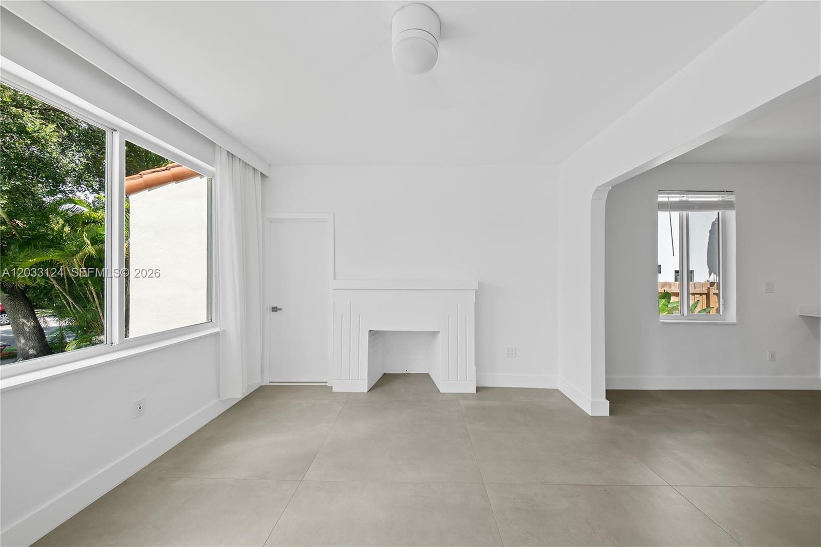 A bright, minimalist living room features a white fireplace, large windows, and gray tile flooring — 565 NW 44th St, Miami FL 33127, MIAMI, FL