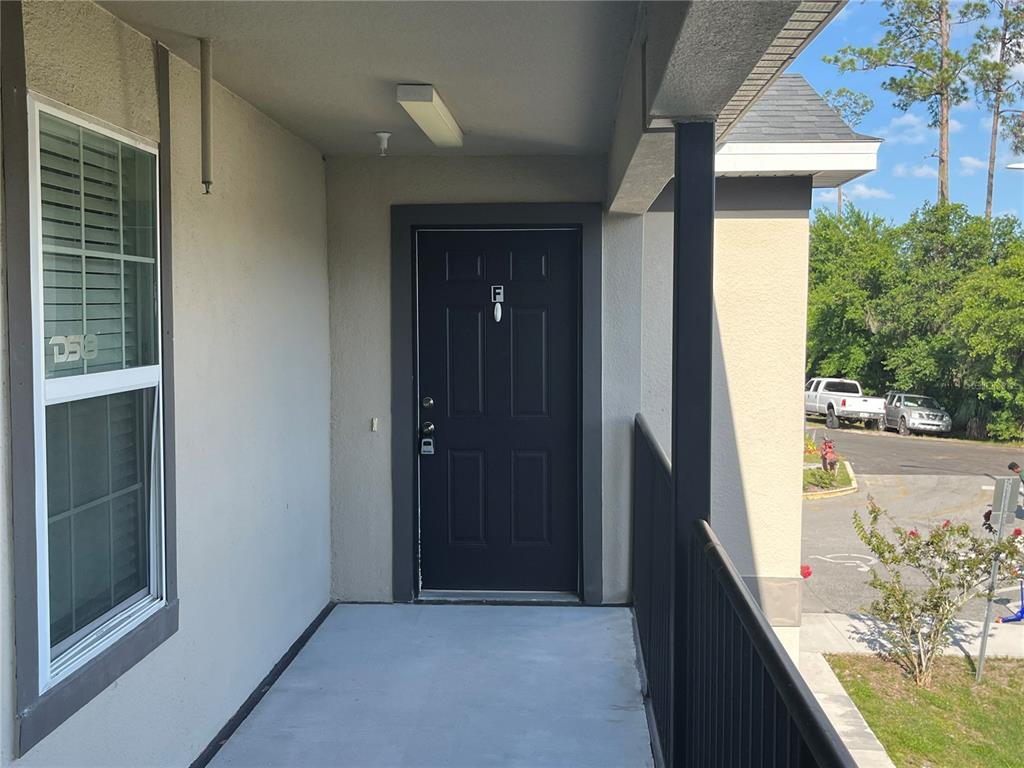 A dark front door with the letter F is located on a covered apartment balcony — 295 FLOWER LANE UNIT F, KISSIMMEE, FL