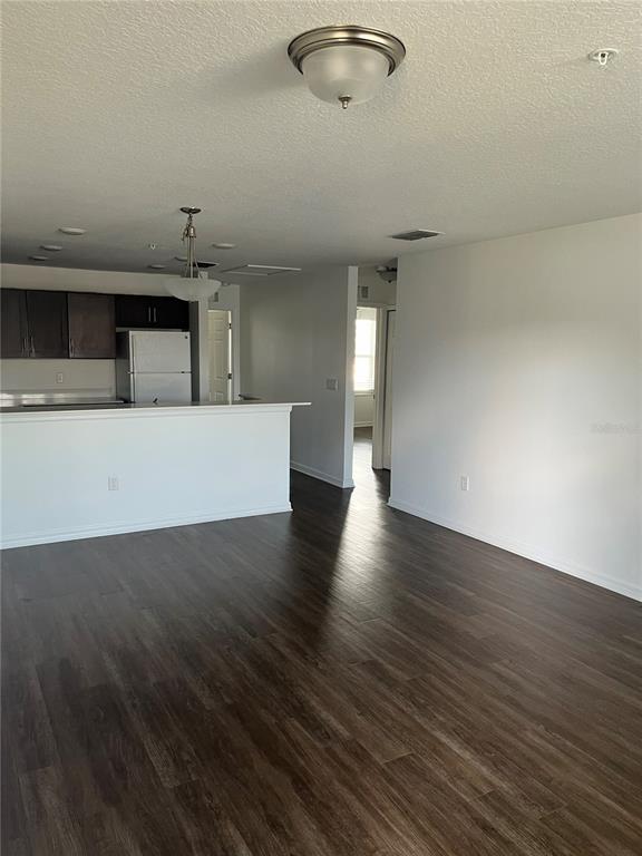 An open-concept living area features dark wood-look flooring, a kitchen island, and white walls — 295 FLOWER LANE UNIT F, KISSIMMEE, FL