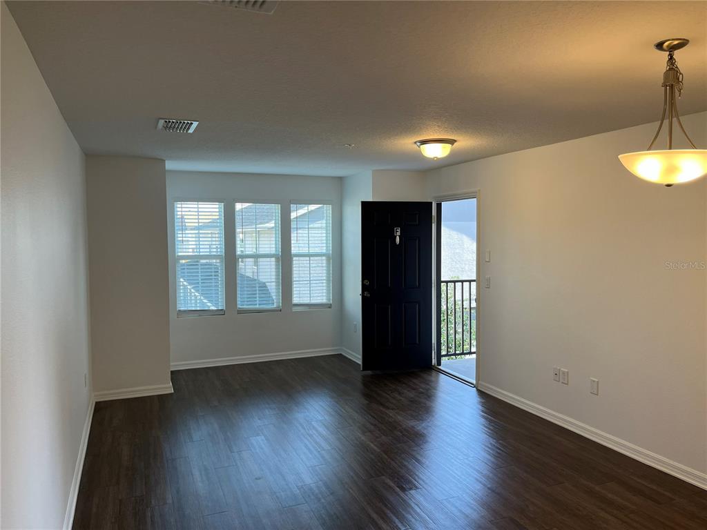 An empty room features dark wood-look flooring, a black front door, and a balcony entrance — 295 FLOWER LANE UNIT F, KISSIMMEE, FL