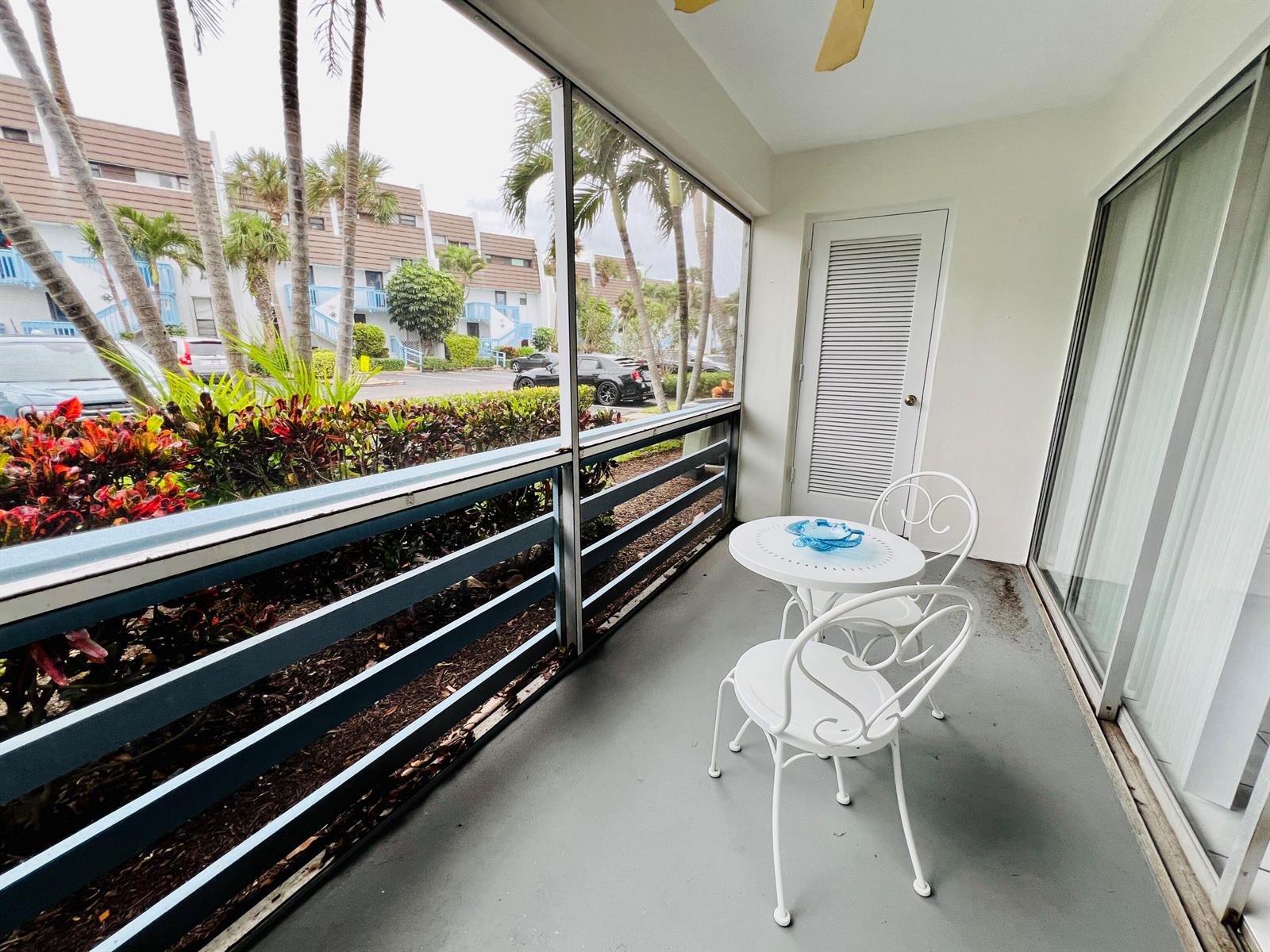 A screened-in balcony features a small white bistro set and views of palm trees — 11000 S Ocean Drive # 2, Jensen Beach FL 34957, JENSEN BEACH, FL