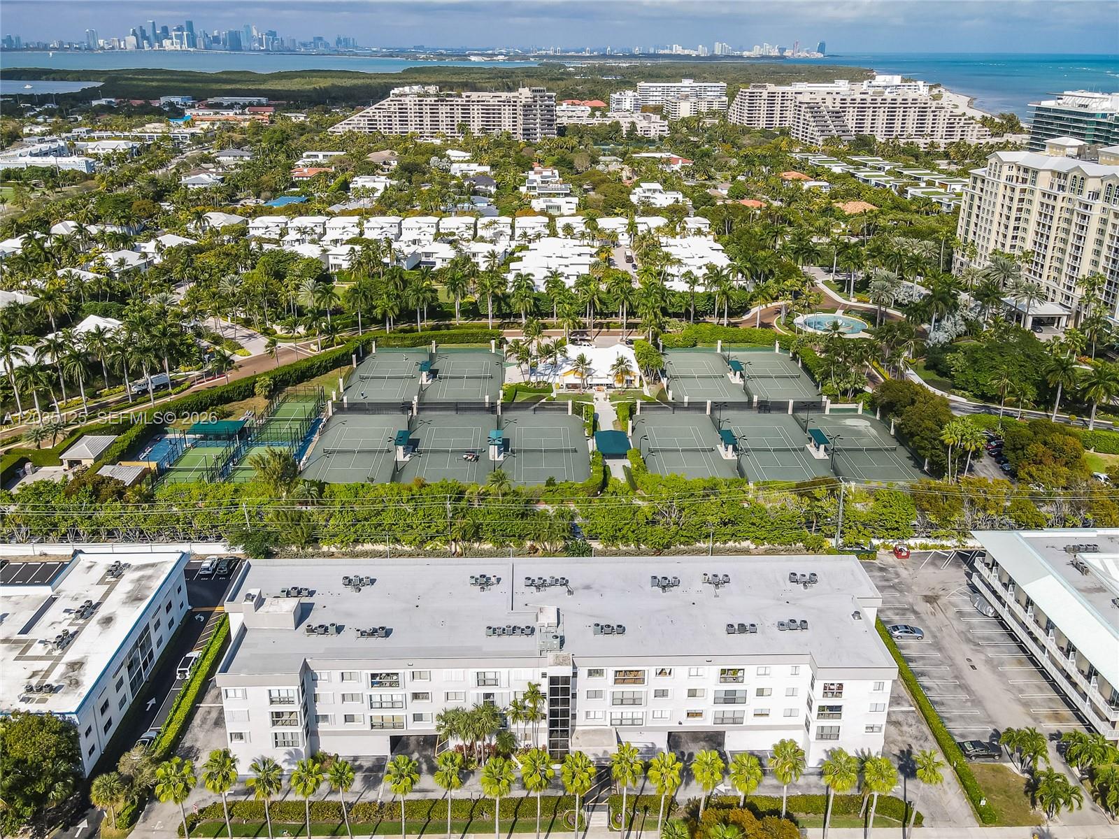 An aerial view shows a multi-story apartment building, tennis courts, and surrounding residential landscaping — KEY BISCAYNE, FL