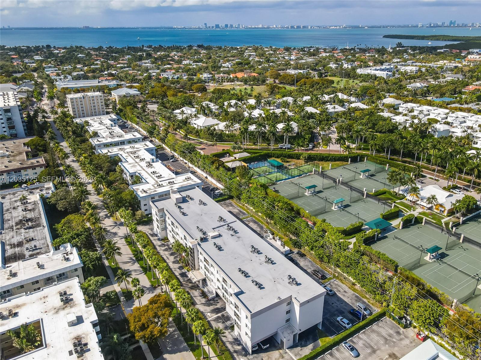 An aerial view shows multi-story residential buildings next to several tennis courts and palm trees — KEY BISCAYNE, FL