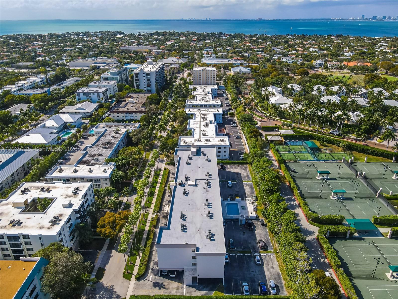 An aerial view shows residential apartment buildings, parking lots, and tennis courts near the coast — KEY BISCAYNE, FL