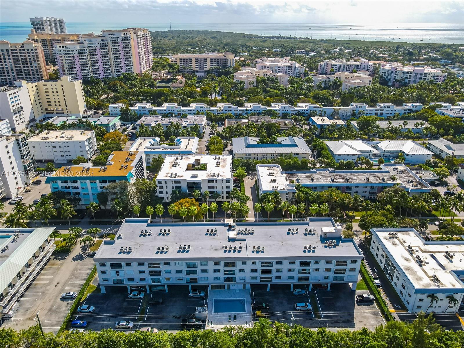An aerial view shows a multi-story apartment complex with a ground-level parking lot and pool — KEY BISCAYNE, FL