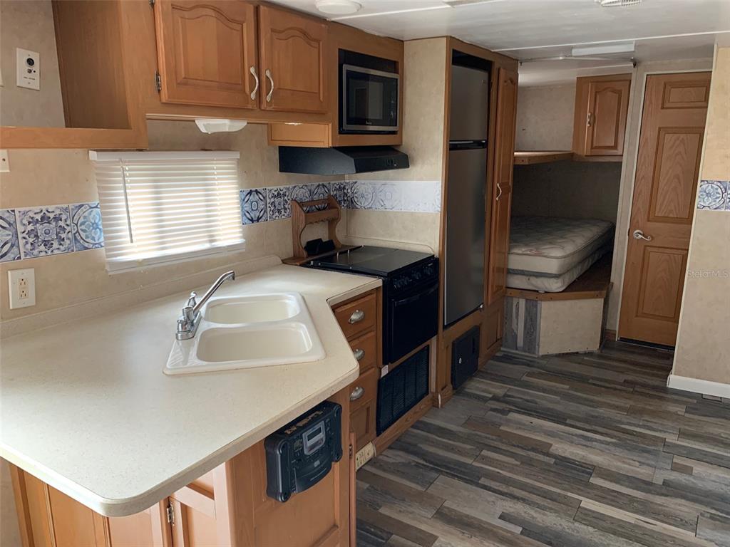 A kitchen with light countertops, wood cabinets, and a stove leads to a small bedroom — 3000 CLARCONA ROAD UNIT 333, APOPKA, FL