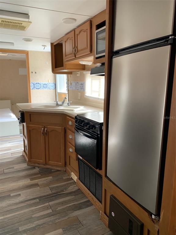 A kitchen with wood cabinets, a stainless steel refrigerator, a black stove, and wood-look flooring — 3000 CLARCONA ROAD UNIT 333, APOPKA, FL