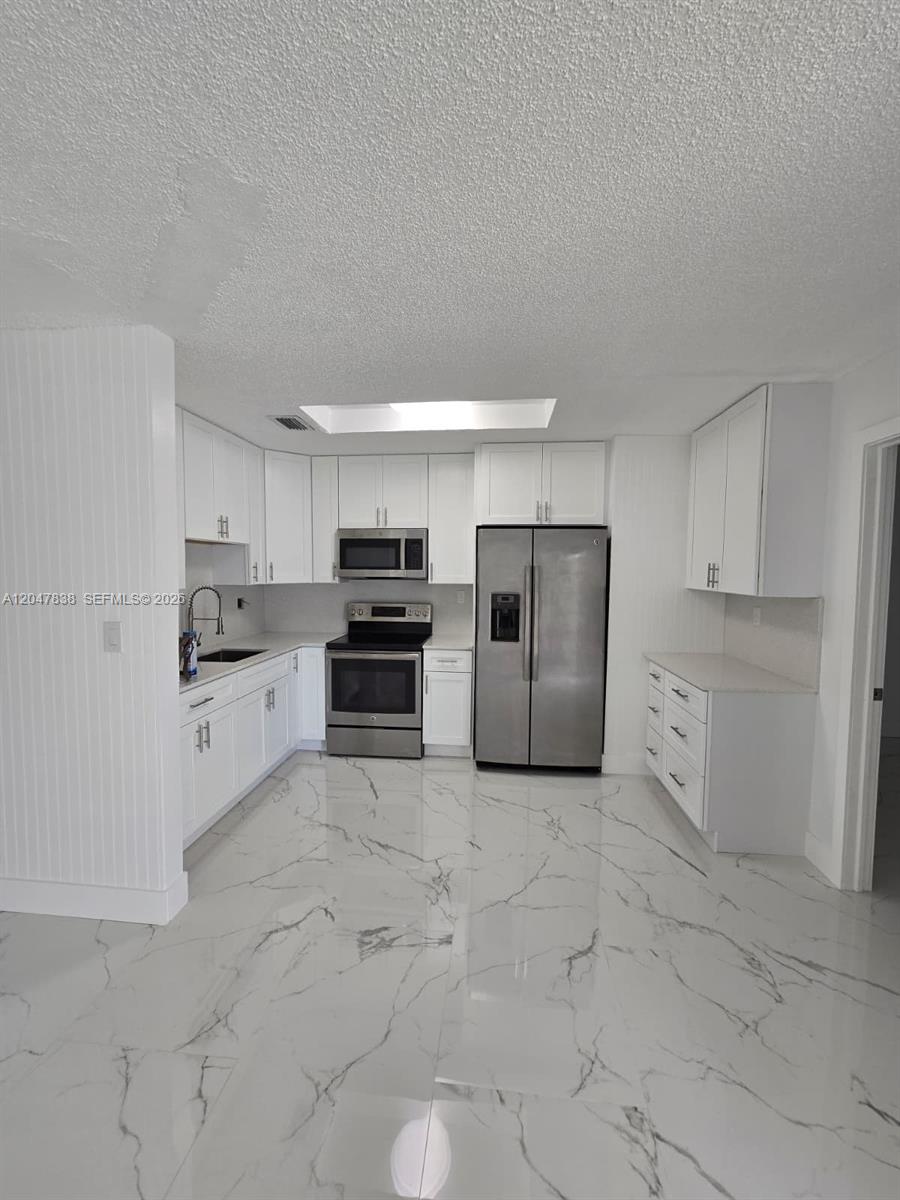 A kitchen features white cabinetry, stainless steel appliances, and white marble-patterned tile flooring — 13470 SW 24th St, Miami FL 33175, MIAMI, FL