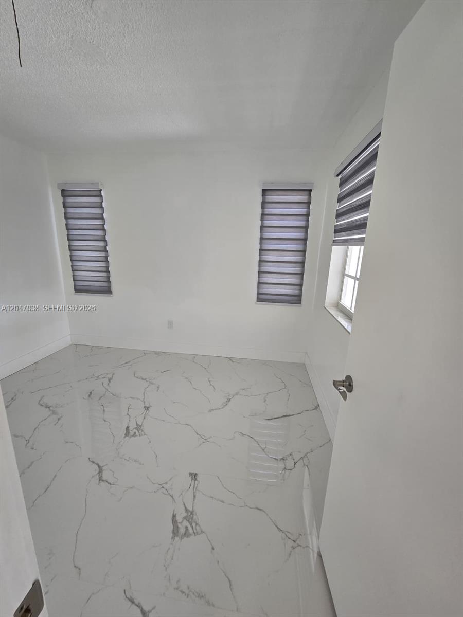A small room features white walls, marble-patterned tile flooring, and two windows with gray blinds — 13470 SW 24th St, Miami FL 33175, MIAMI, FL