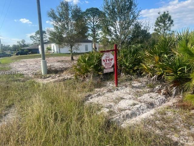 A vacant lot features a real estate sign and sparse vegetation in front of a house — 2708 38 ST W, Lehigh Acres FL 33971, LEHIGH ACRES, FL