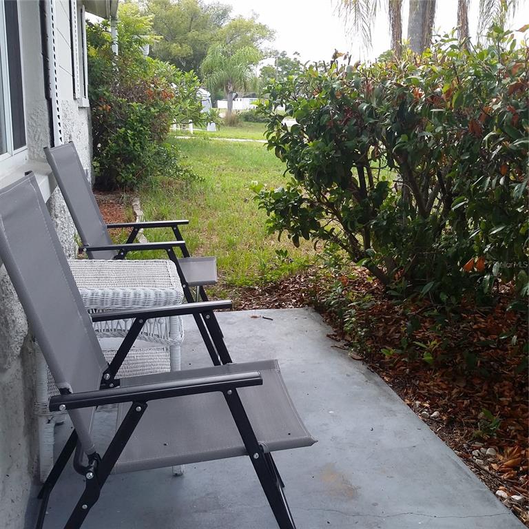 Two gray folding chairs sit on a concrete patio next to a white wicker table — 7725 ROTTINGHAM ROAD, PORT RICHEY, FL