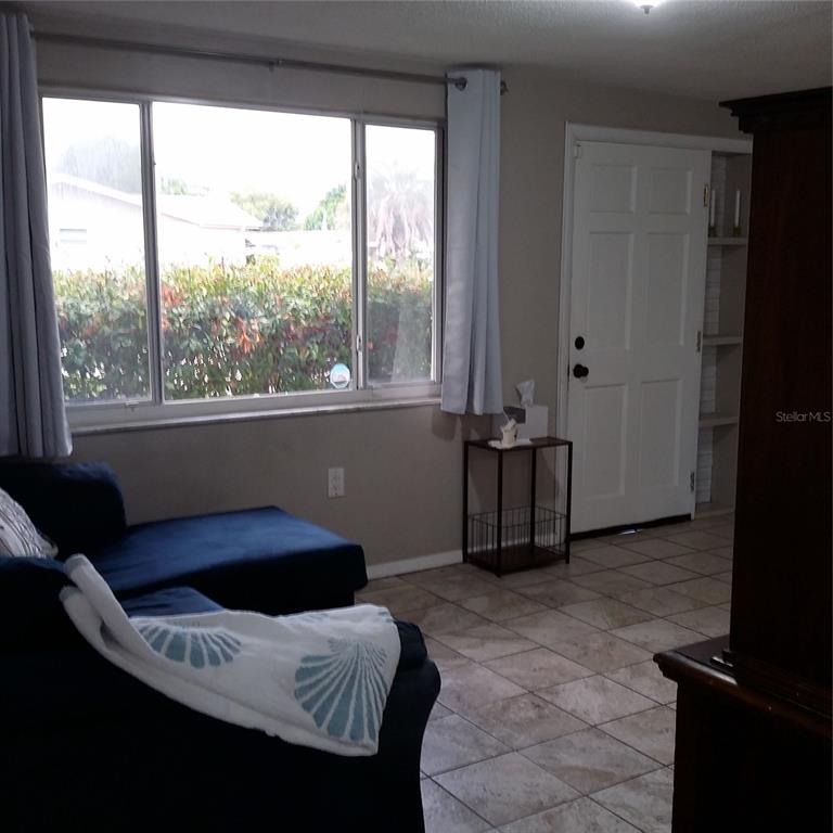 A living room features a blue sectional sofa, a large window, and a white door — 7725 ROTTINGHAM ROAD, PORT RICHEY, FL