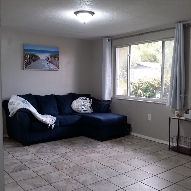 A living room features a blue sectional sofa, tiled floors, and a large window — 7725 ROTTINGHAM ROAD, PORT RICHEY, FL