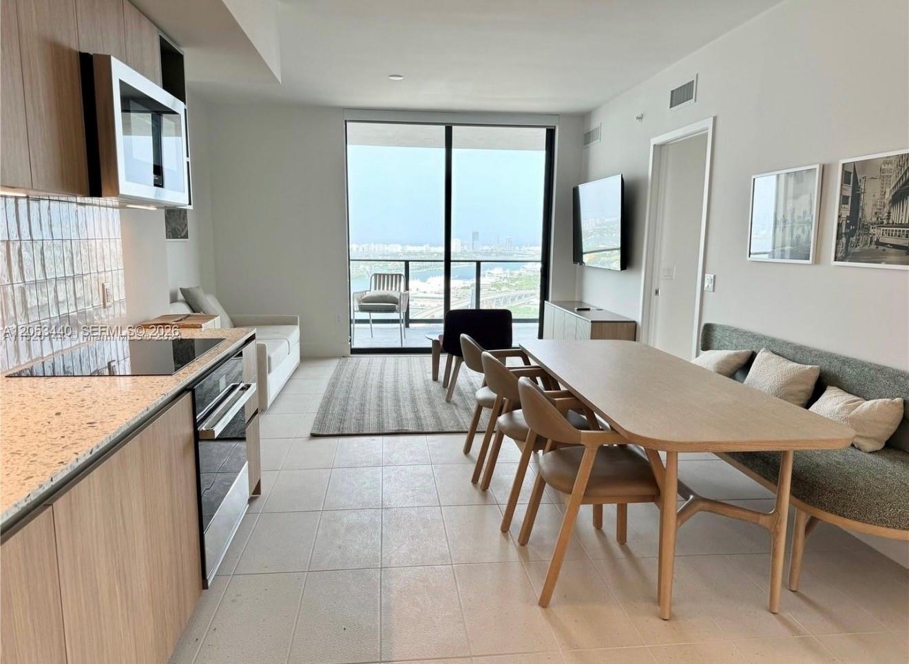 A modern open-concept apartment features a kitchen, dining area, and balcony with a city view — 159 NE 6th St # 3215, Miami FL 33132, MIAMI, FL
