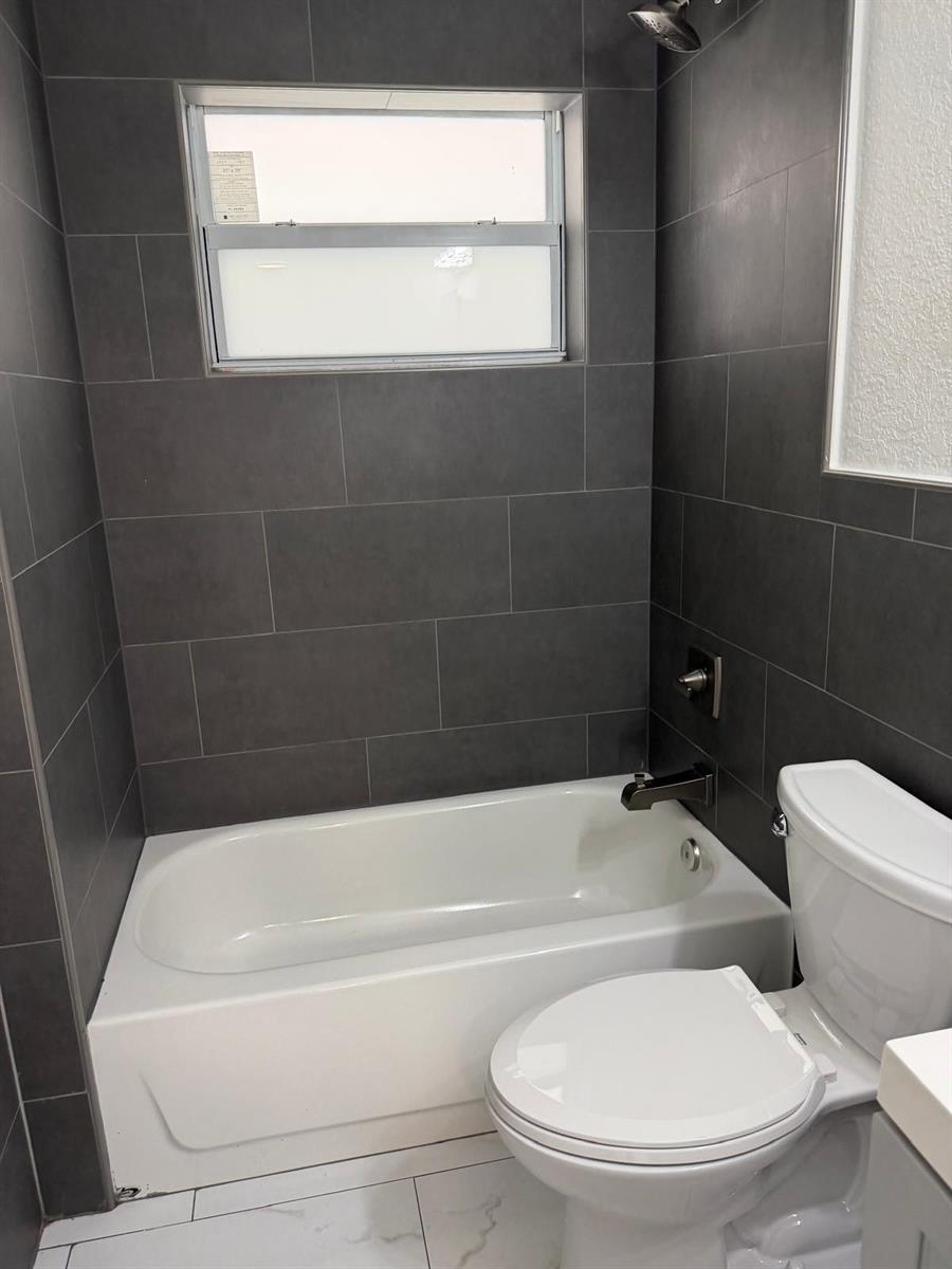 A bathroom features a white bathtub, a toilet, and dark gray tiled shower walls — 110 NW 7th Avenue # 18, Pompano Beach FL 33060, POMPANO BEACH, FL