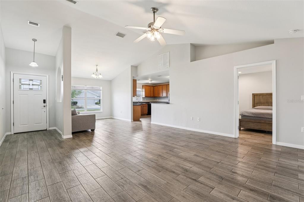 An open-concept living area features wood-look tile flooring, a vaulted ceiling, and a kitchen view — 264 CHICAGO AVENUE W, HAINES CITY, FL