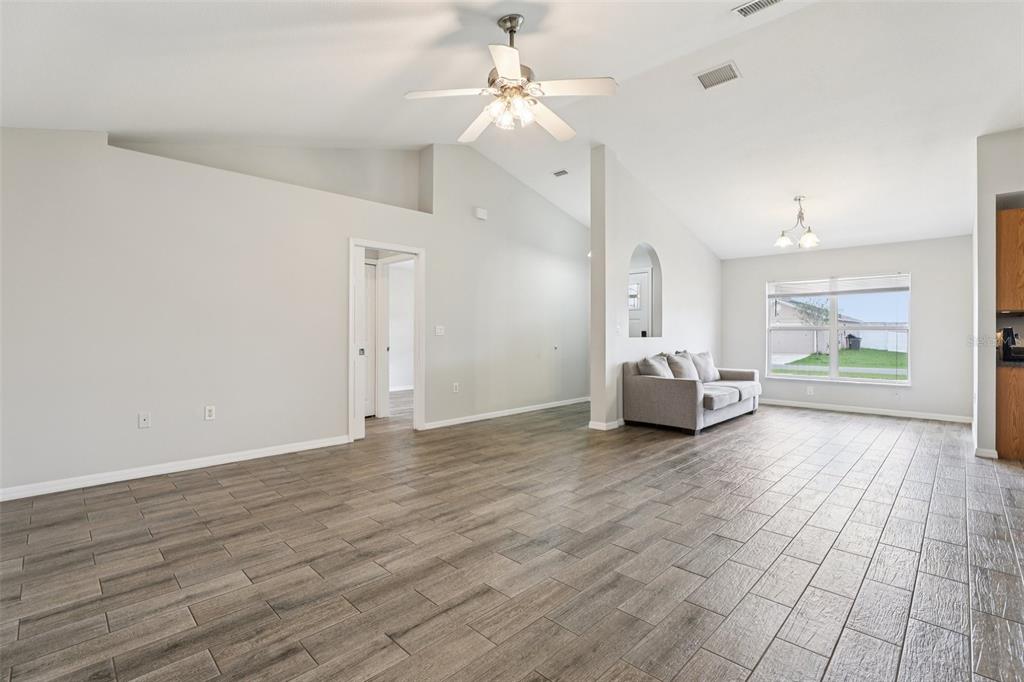 A spacious living room features vaulted ceilings, wood-look tile flooring, and a ceiling fan — 264 CHICAGO AVENUE W, HAINES CITY, FL