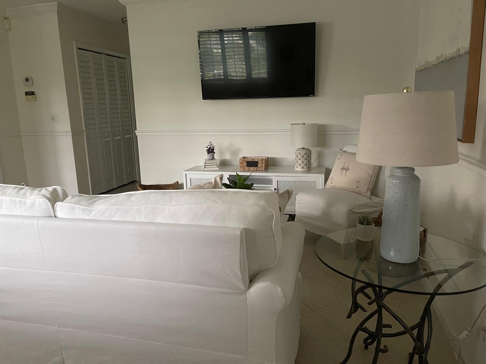 A bright living room features a white sofa, a television, and a glass-topped side table — 1202 Palm Trail # 6, Delray Beach FL 33483, DELRAY BEACH, FL