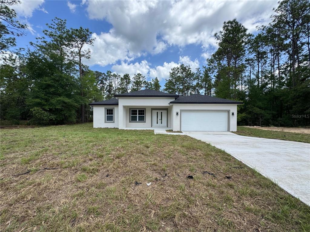 A single-story white house with a two-car garage sits on a grassy lot with trees — 2523 W ANDROMEDAE DRIVE, CITRUS SPRINGS, FL