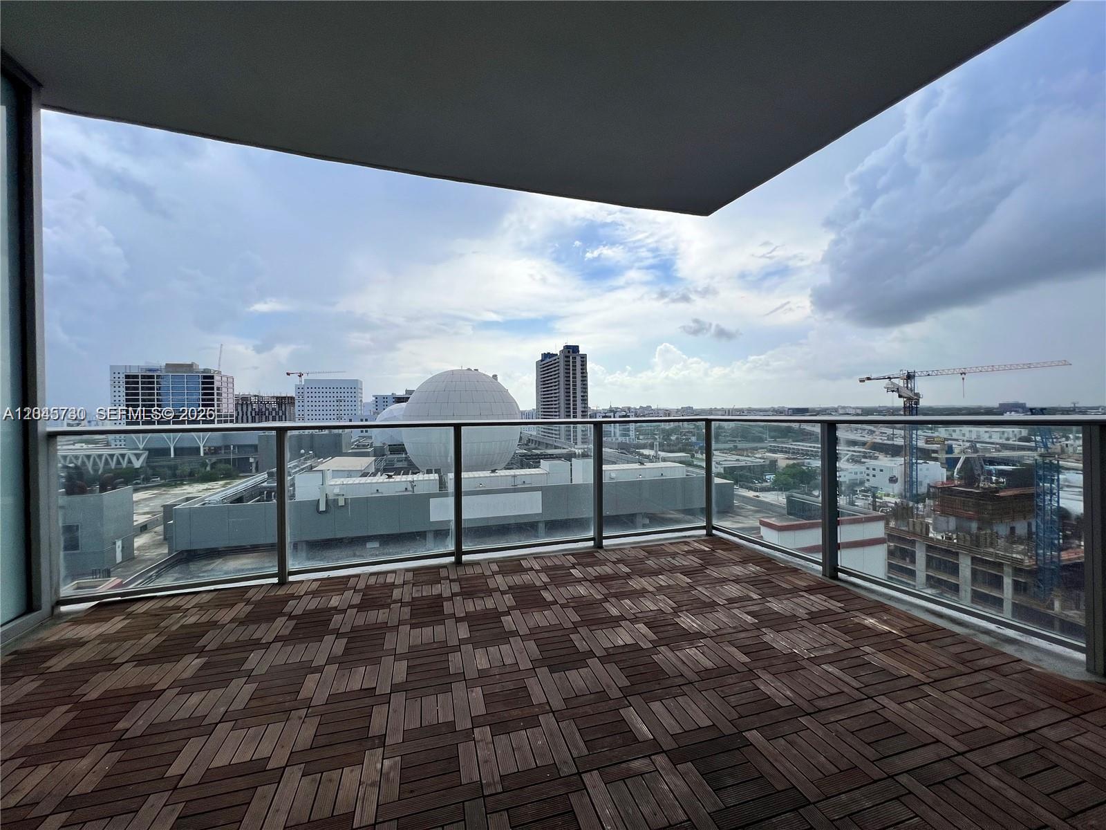 A balcony with wood-tiled flooring overlooks a city skyline featuring a large spherical structure — 851 NE 1st Ave # 1208, Miami FL 33132, MIAMI, FL
