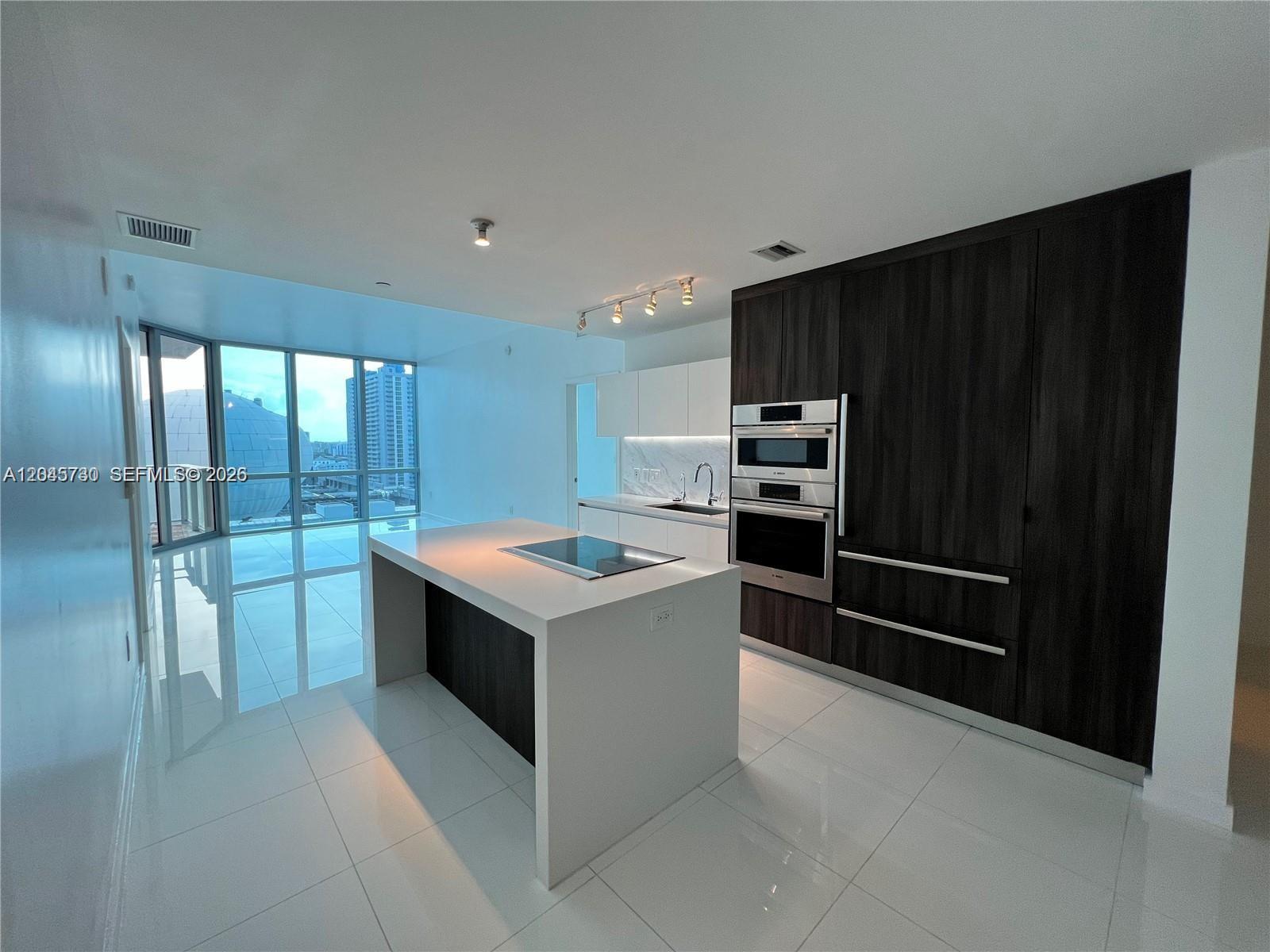 A modern kitchen features a white island, dark wood cabinetry, and floor-to-ceiling windows — 851 NE 1st Ave # 1208, Miami FL 33132, MIAMI, FL