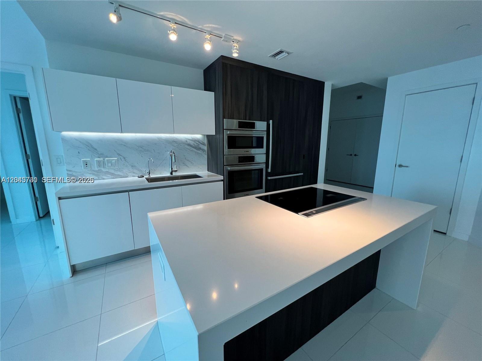 A modern kitchen features white cabinetry, a marble backsplash, and a large central island — 851 NE 1st Ave # 1208, Miami FL 33132, MIAMI, FL