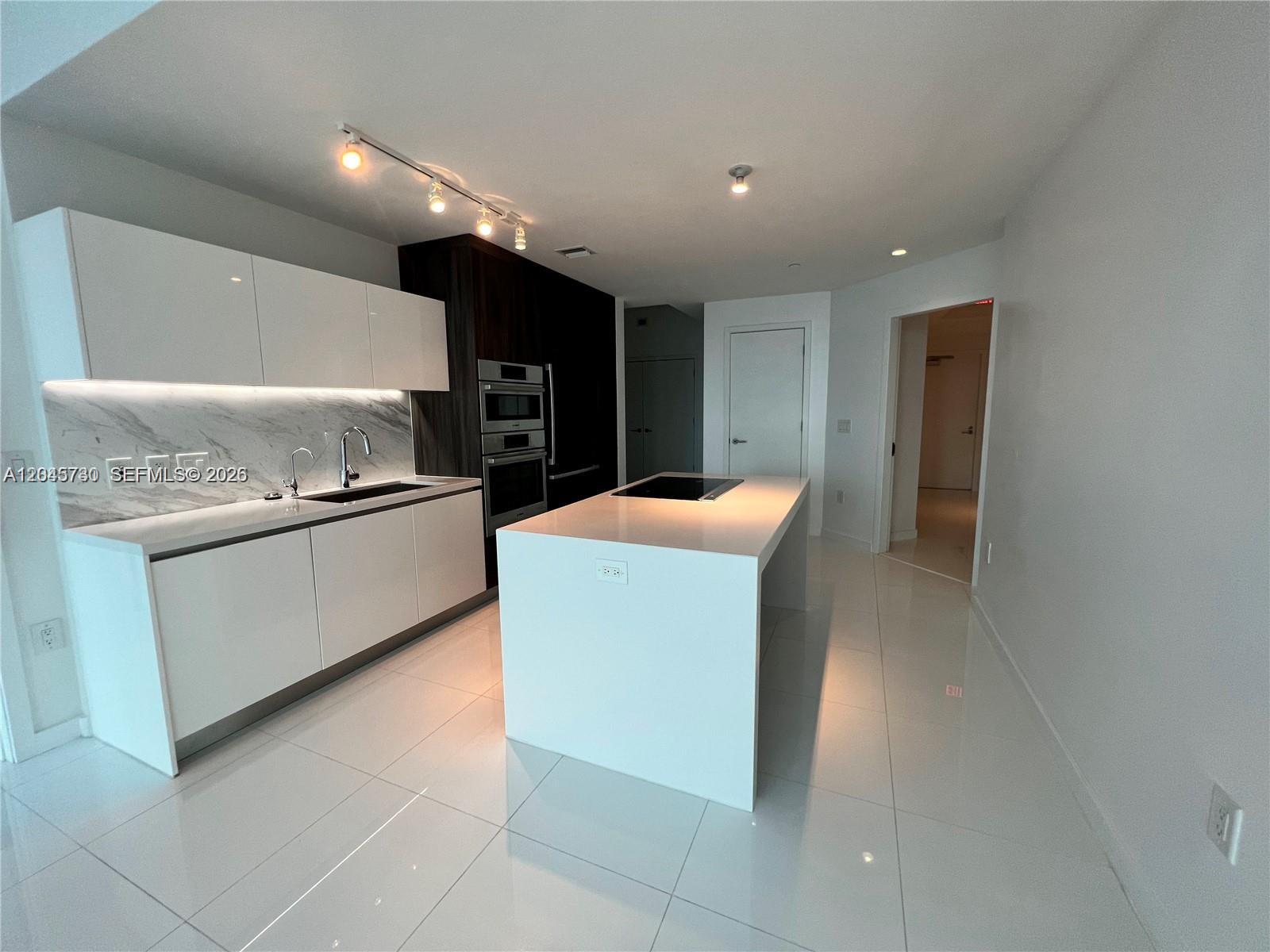 A modern kitchen features white cabinetry, a marble backsplash, and a central island with a cooktop — 851 NE 1st Ave # 1208, Miami FL 33132, MIAMI, FL