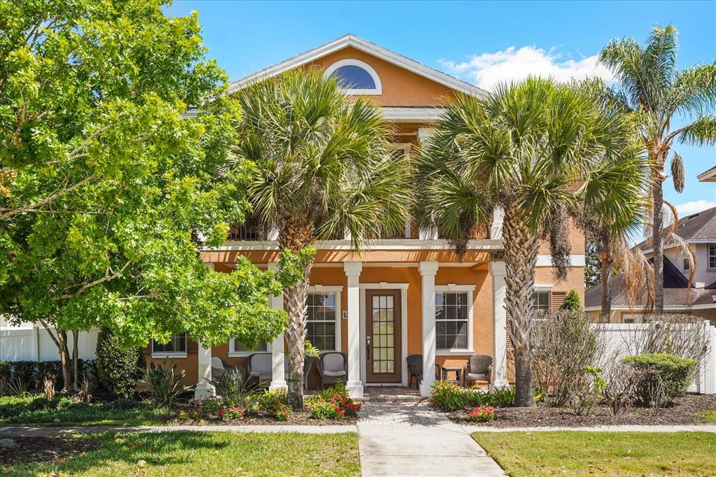 A two-story orange house with a front porch, columns, and palm trees in the yard — 7708 EXCITEMENT DRIVE, REUNION, FL